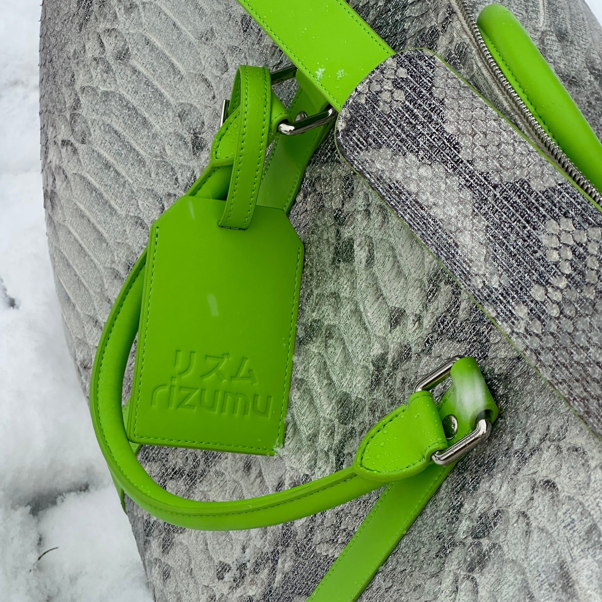 Silver python travel bag with lime leather straps and an embossed rizumu tag, photographed in snow